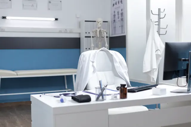 Mesa de consultório com computador e cadeira.