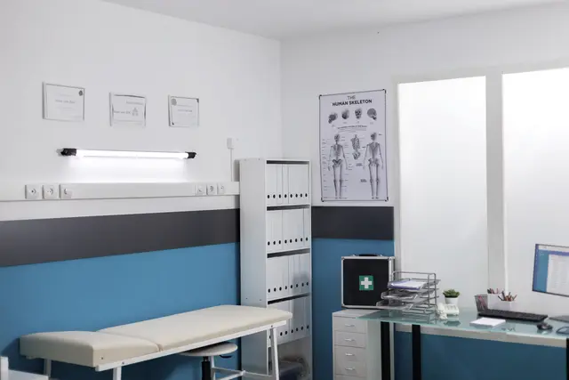 Consultório médico com maca e mesa de atendimento.