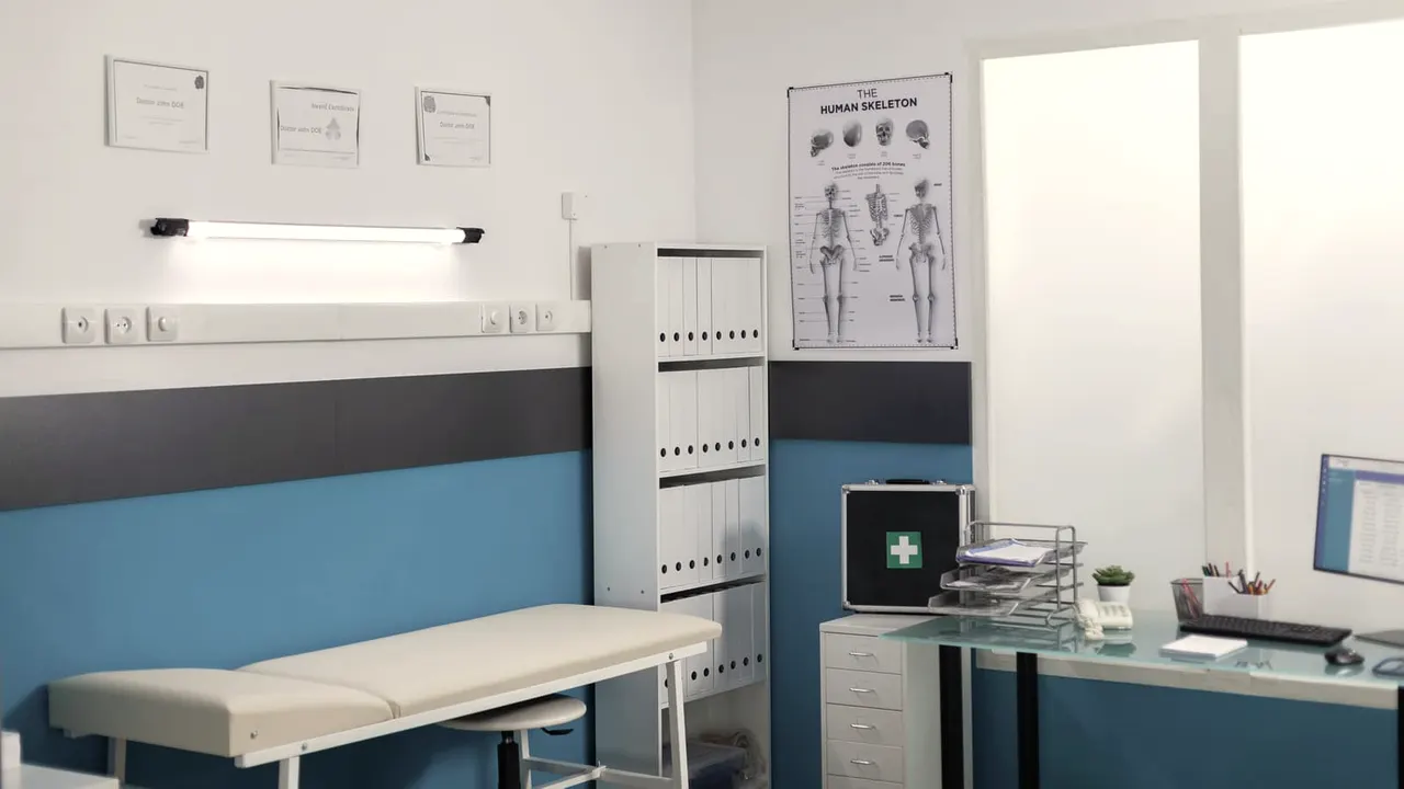 Consultório médico claro com maca e mesa de atendimento.