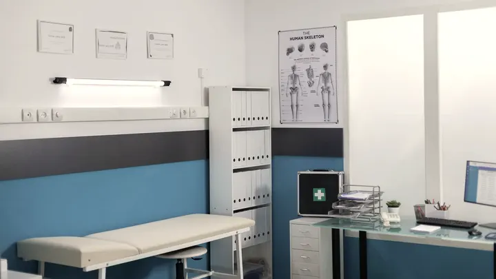 Consultório médico claro com maca e mesa de atendimento.