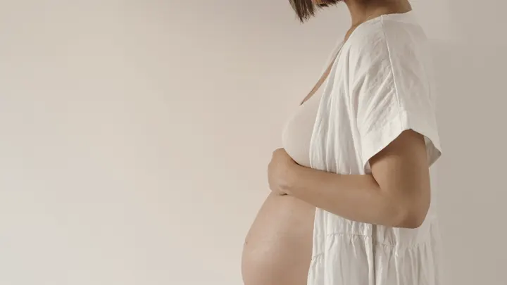 Gestante de branco tocando a barriga, retrato minimalista.