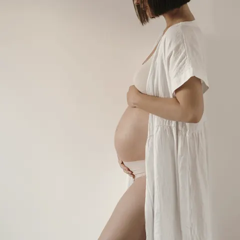 Gestante de branco tocando a barriga, retrato minimalista.